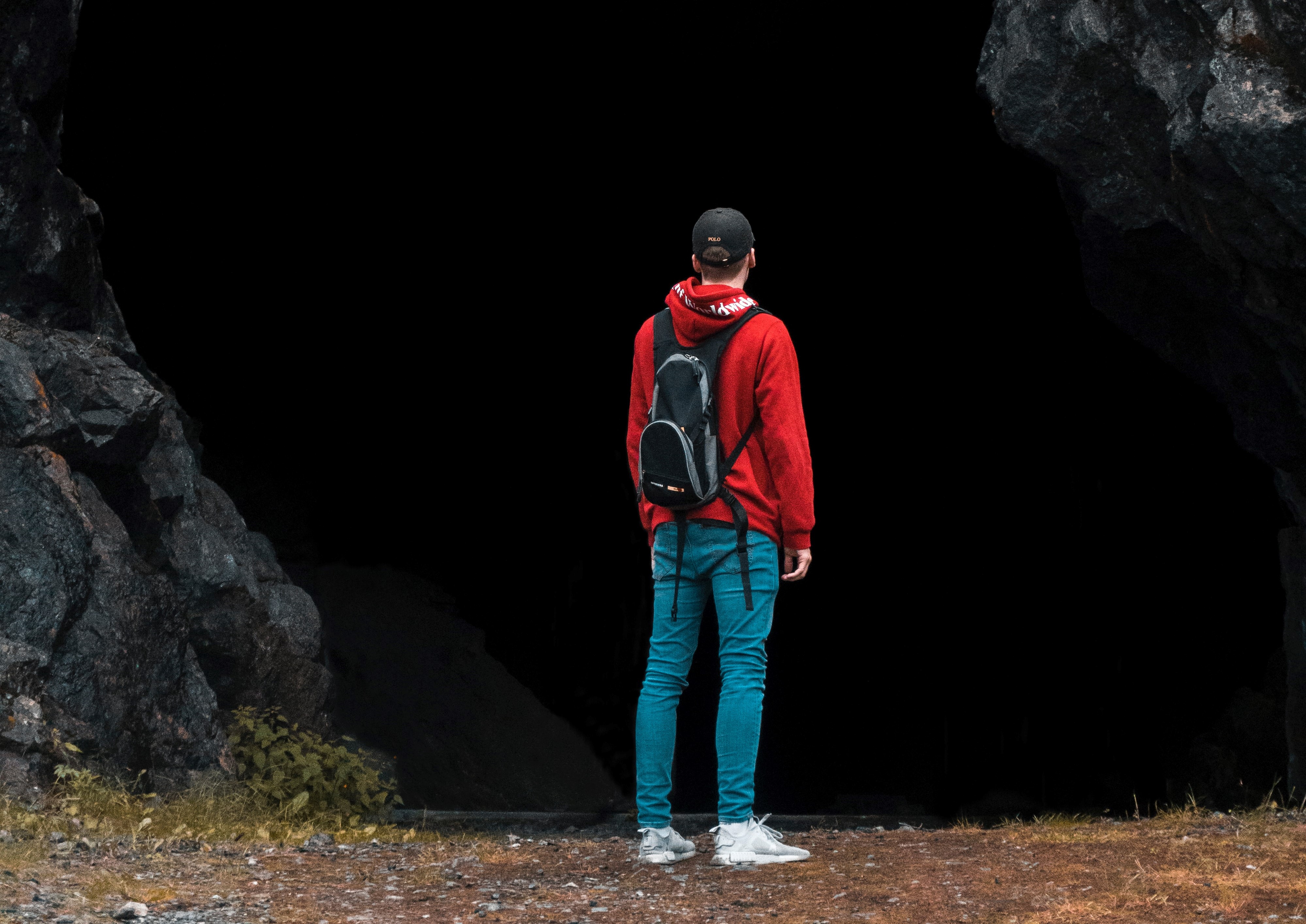 a man in a red hoodie stands in the mouth of a giant cave